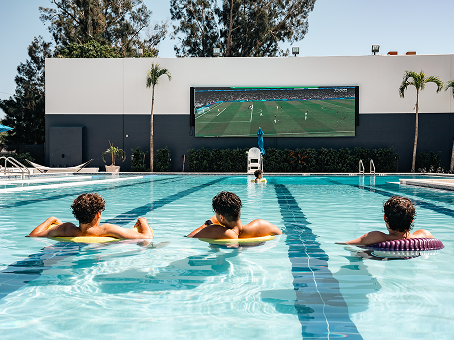 Students watch jumbo tv of sports game while floating in new college pool