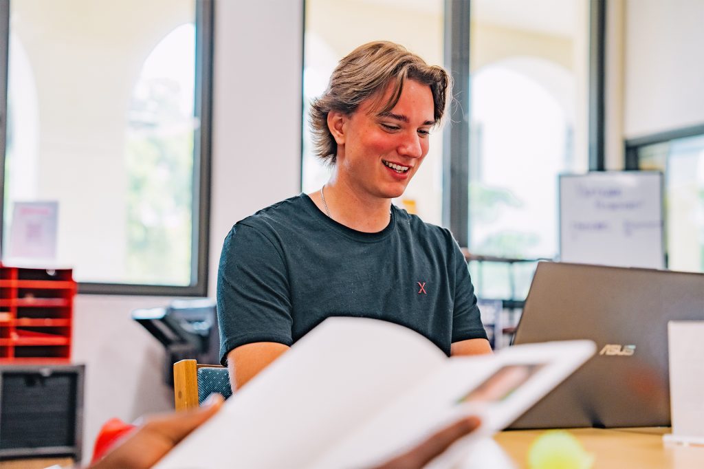 Student laughing in office with an open notebook in the foreground